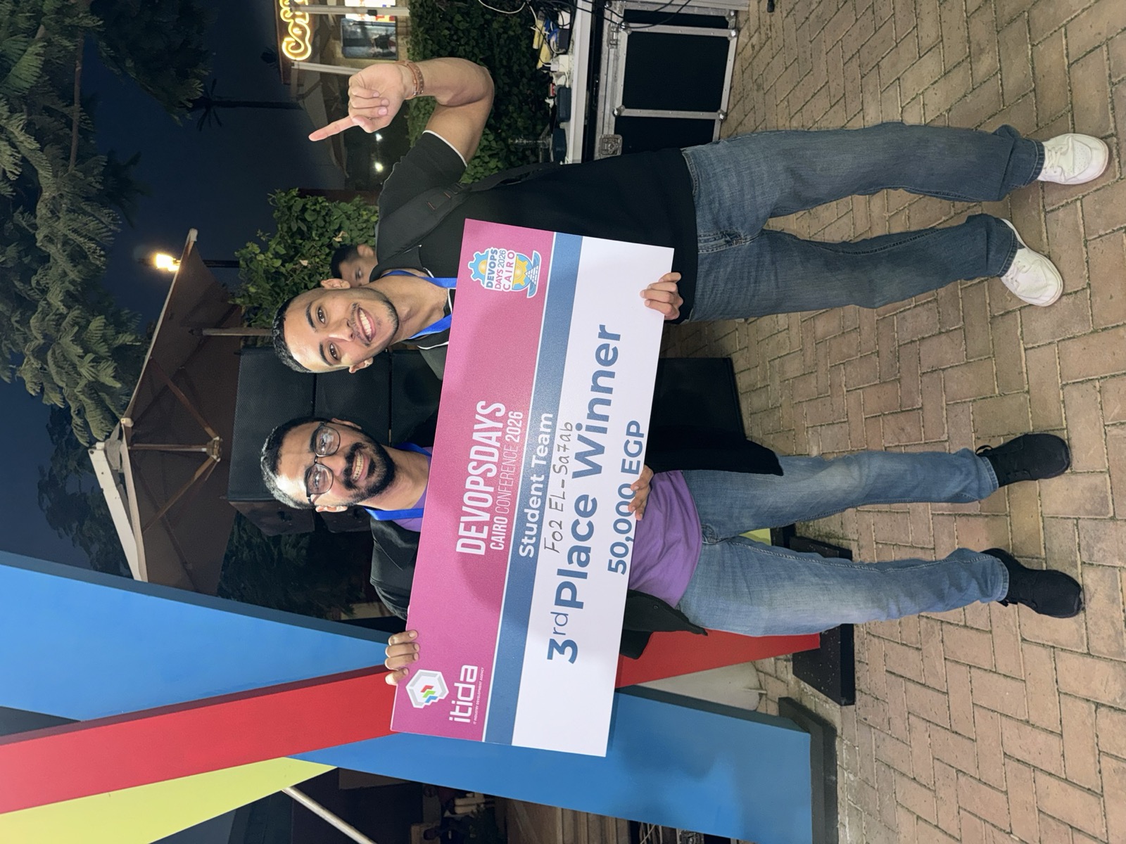 Ahmed and a teammate holding the DevOpsDays Cairo 2026 third-place cheque for 50,000 EGP